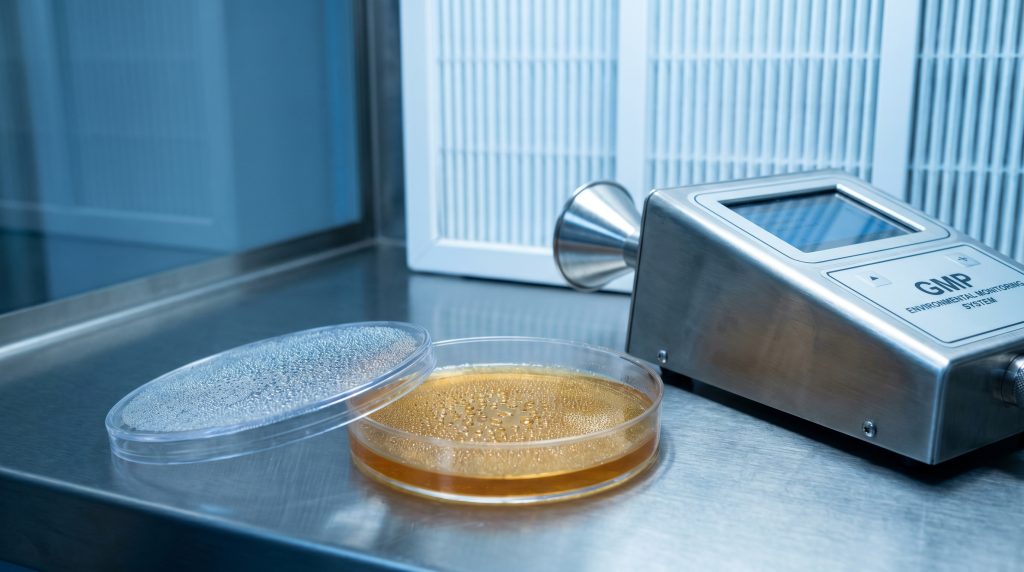 Microbiologische kwaliteitscontrole in een laboratorium volgens GMP-richtlijnen met een deeltjesteller en een petrischaal.